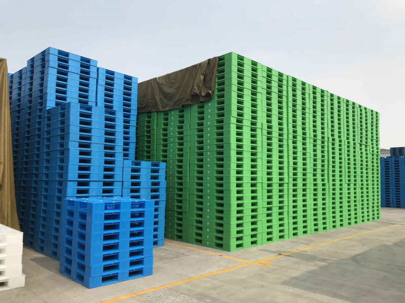 Stacked blue and green double-sided plastic pallets in outdoor factory yard for bulk storage