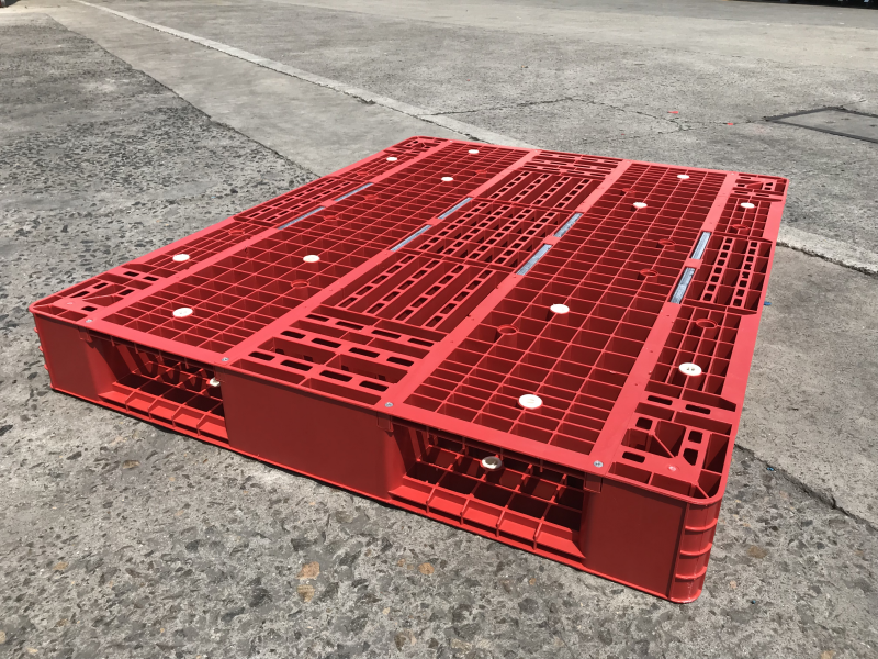 Red grid reversible plastic pallet with full deck and built-in steel bars on outdoor concrete ground